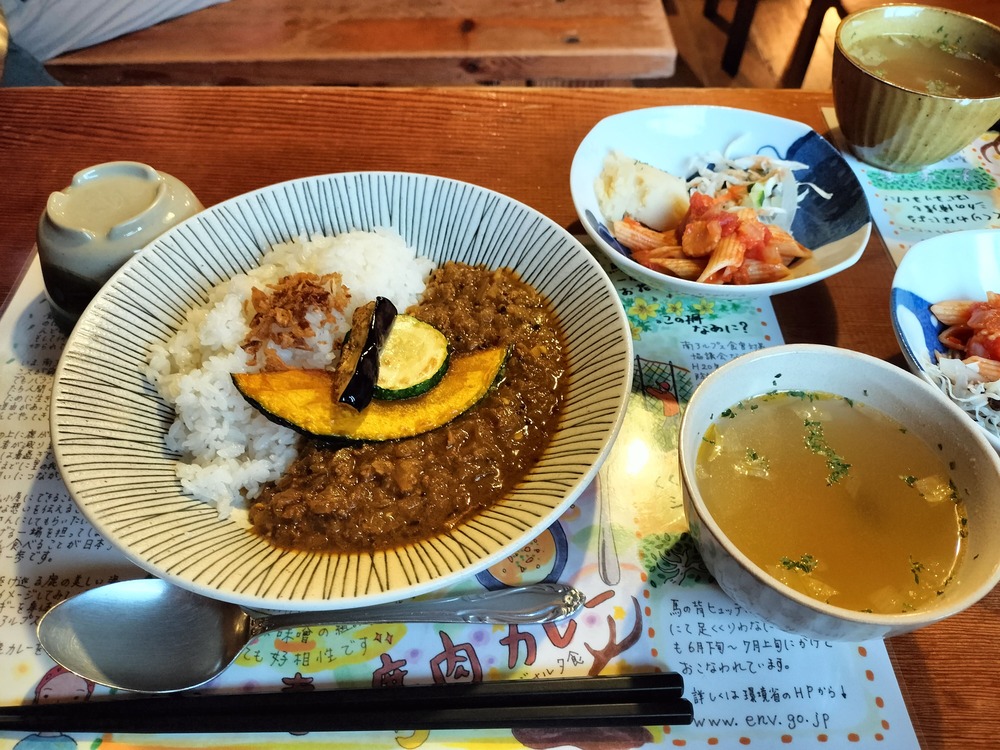 鹿肉のジビエカレー。大きな焼き野菜が上に乗っており、副菜にコンソメスープもついている
